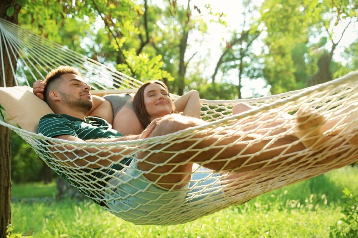 Junges Paar ruht sich in einer bequemen Hängematte in einem grünen Garten aus