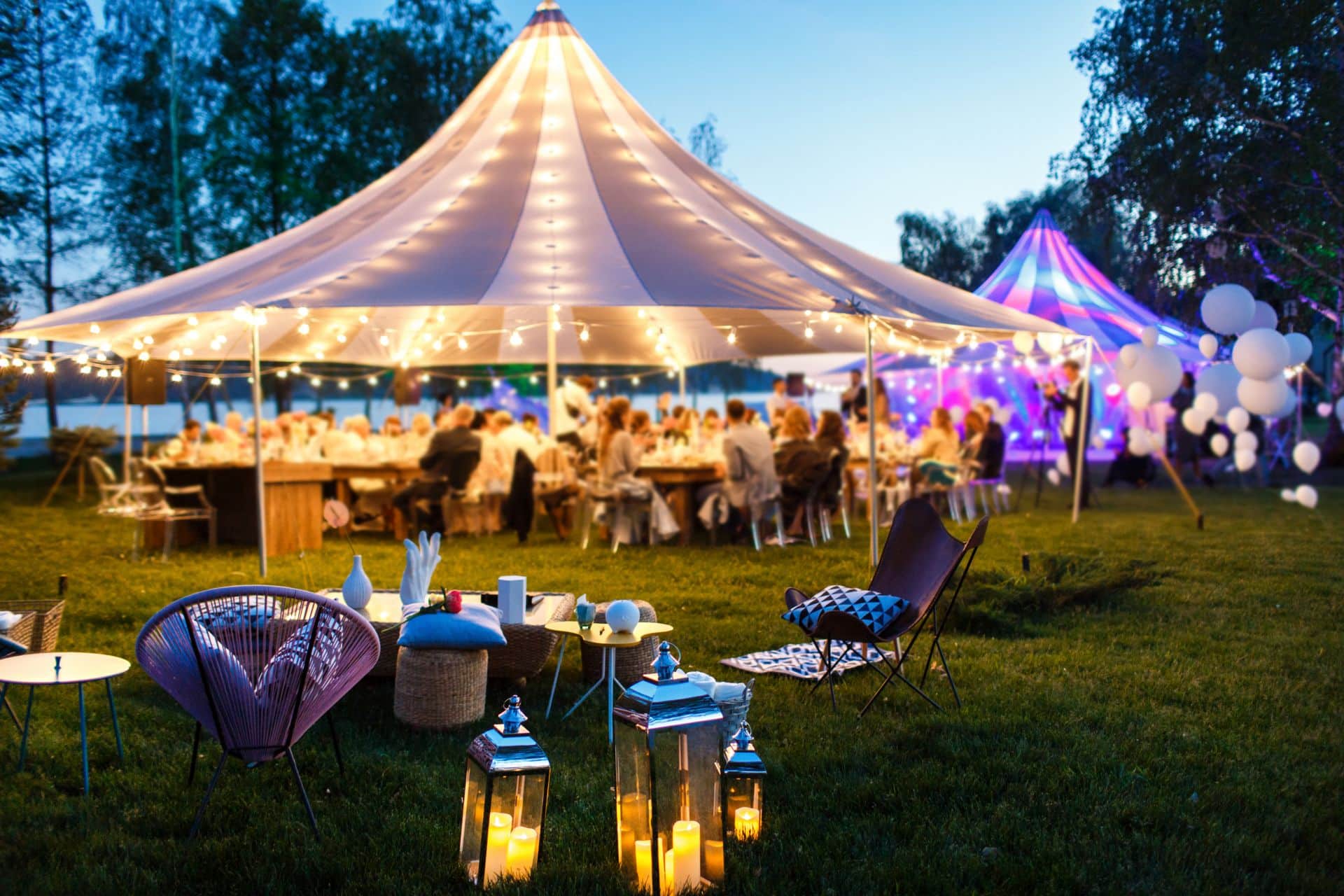 Ein stilvoll beleuchteter Pavillon bei einer abendlichen Gartenfeier, umgeben von Gästen und dekorativen Laternen.