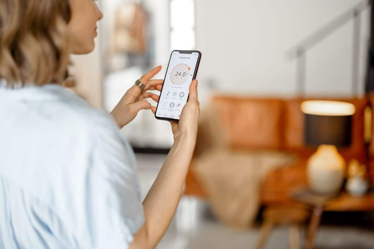 Woman adjusting home temperature on smartphone app, displaying data from airflow sensors for climate control