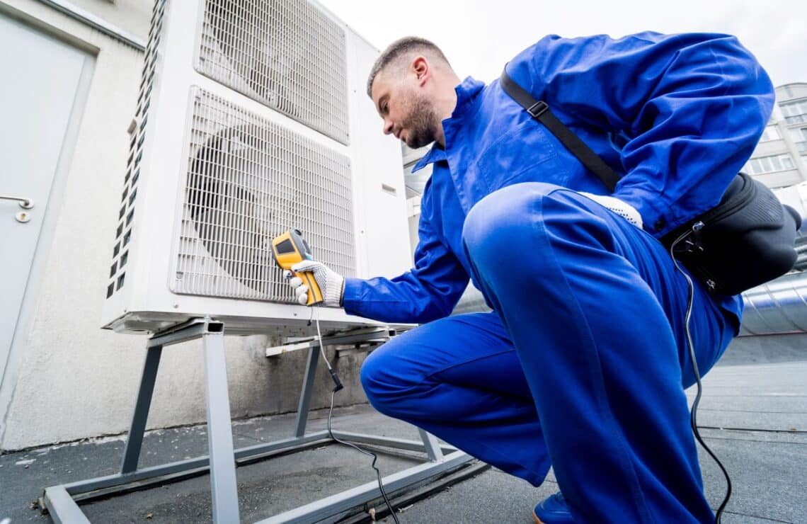 Technician in blue uniform measuring the temperature of an HVAC unit to ensure proper function of airflow sensors