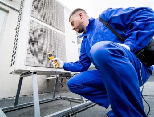 Technician in blue uniform measuring the temperature of an HVAC unit to ensure proper function of airflow sensors