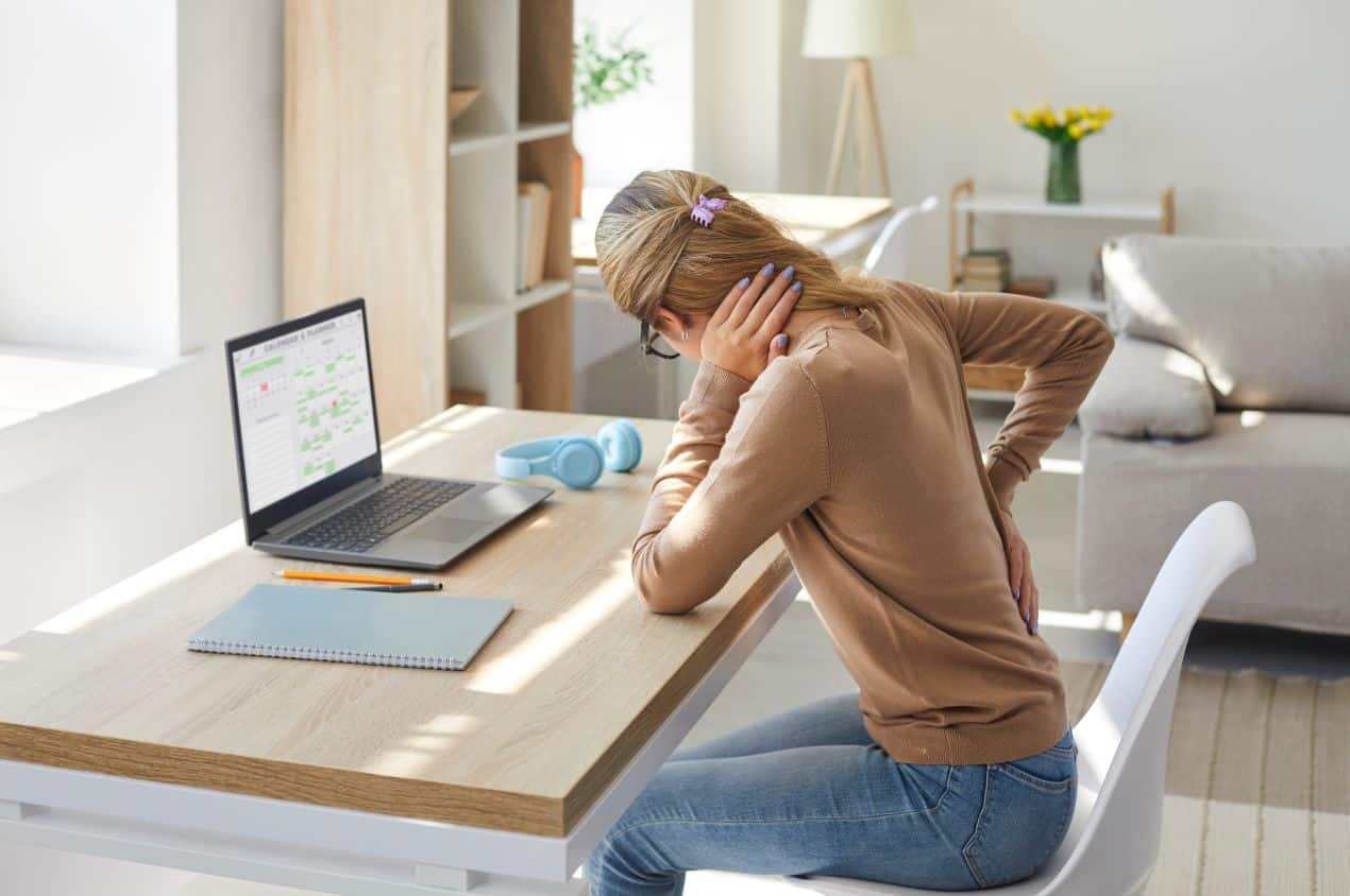 Junge Frau mit Ruecken- und Nackenschmerzen am Schreibtisch – typischer Anlass fuer eine Untersuchung in der Radiologie Duesseldorf