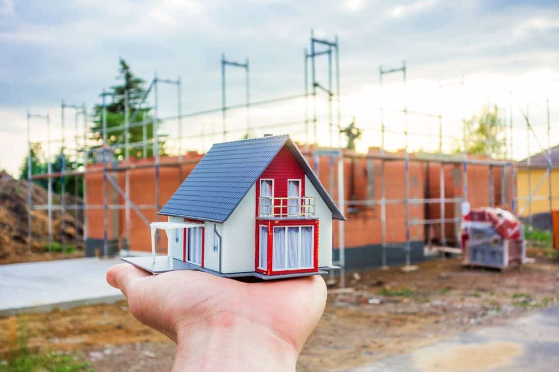 Hausmodell auf Hand vor Neubau | Scherenbühnen mieten
