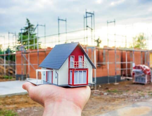 Hausmodell auf Hand vor Neubau | Scherenbühnen mieten