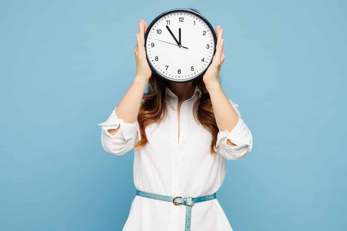 Frau verdeckt Gesicht mit Uhr vor blauem Hintergrund | Arbeitsrecht Tauberbischofsheim