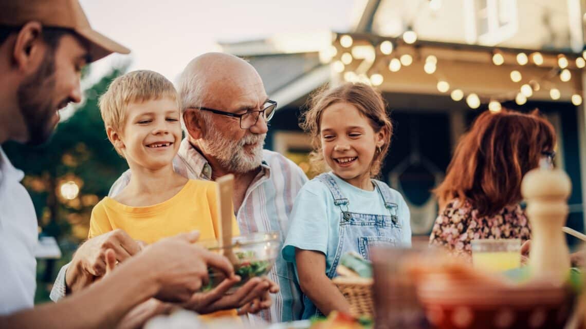 Großvater lacht mit seinen Enkeln bei gemütlichem Familienessen | Bierbank