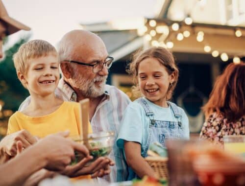 Großvater lacht mit seinen Enkeln bei gemütlichem Familienessen | Bierbank