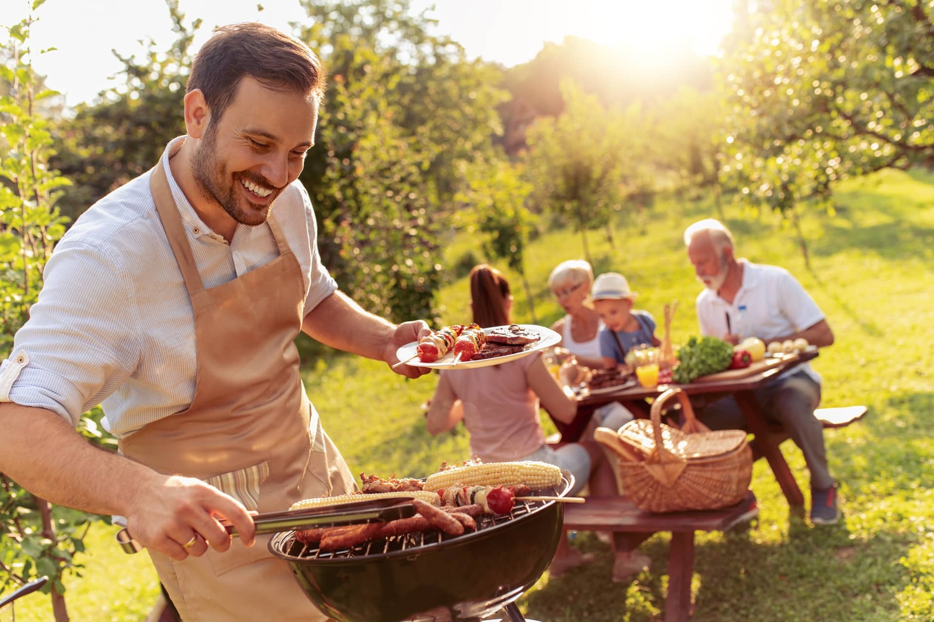 Mann grillt Fleisch und Gemüse bei sommerlicher Gartenfeier | Bierbank